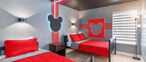 A bedroom with two beds, red bedding, and Mickey Mouse wall decorations.