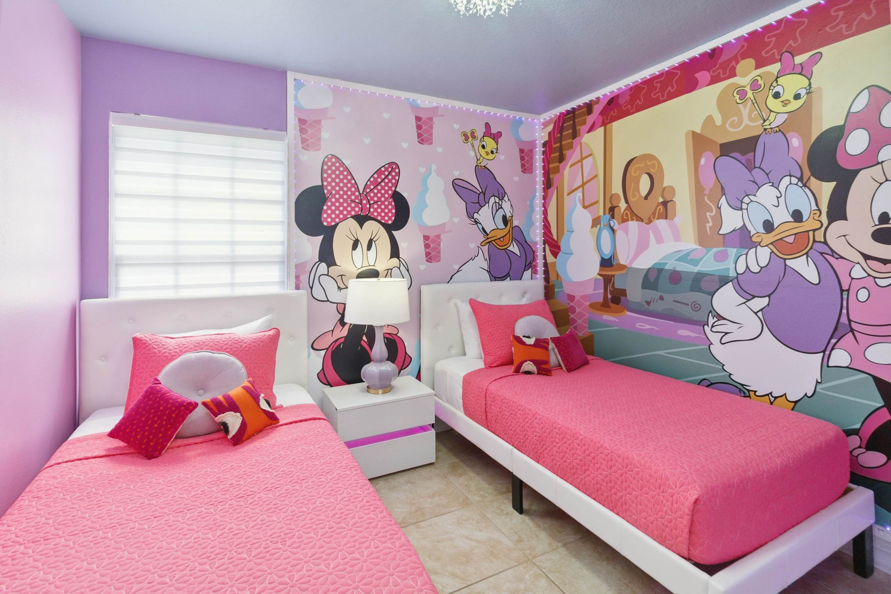 A children's room with two beds, pink bedding, and cartoon character wall art.