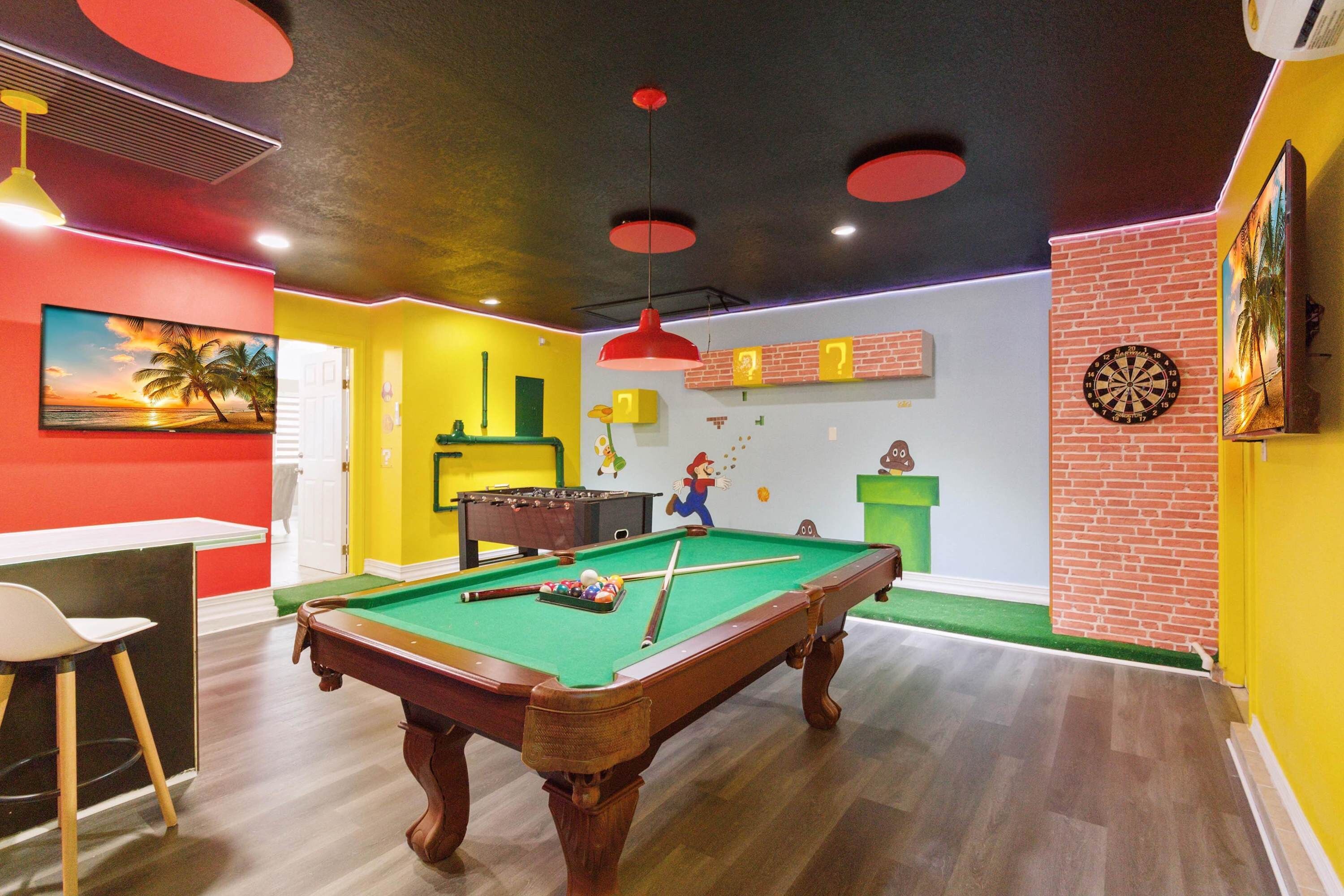 A billiards table in a room with a red and yellow color scheme, a foosball table, and a dartboard.