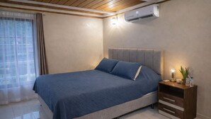 Ein Schlafzimmer mit Bett, Nachttisch, Spiegel, Topfpflanze und Klimaanlage.