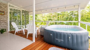 Ein überdachter Außenbereich mit Whirlpool, weißen Stühlen und einer Holzterrasse.