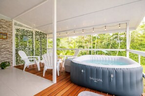 Ein überdachter Außenbereich mit Whirlpool, weißen Stühlen und einer Holzterrasse.