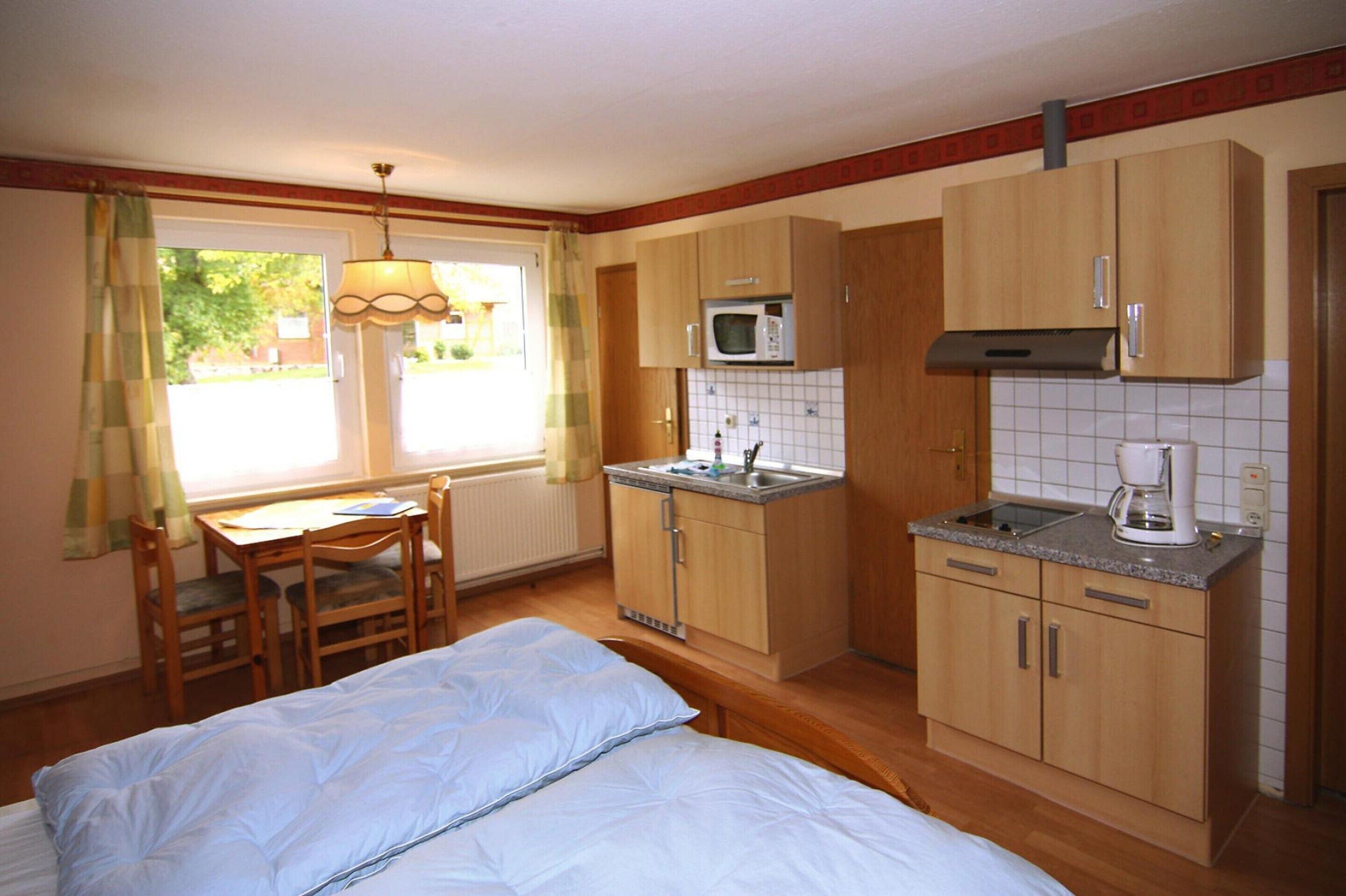 A compact room with a bed, a small dining table, a kitchenette with a microwave and coffee maker, and a window with curtains.