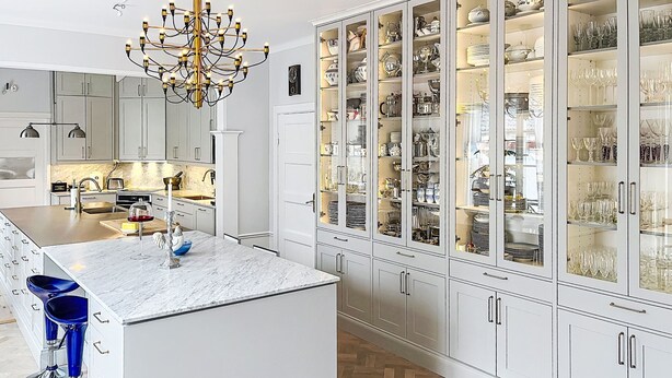 Eine moderne Küche mit einer Marmorinsel, einem Chandelier und einem gläsernen Schrank voller Geschirr und Gläser.