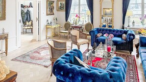 Ein geräumiges Wohnzimmer mit einem blauen Sofa, einer Chandelier und einem großen Spiegel.
