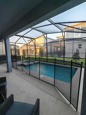 Ein überdachter Außenbereich mit Swimmingpool, einer Terrasse mit Stühlen und Blick auf ein Haus im Hintergrund.