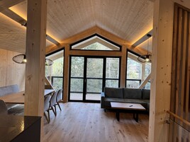 Una habitación amplia con techo alto, vigas de madera, un ventanal grande, un sofá, una mesa y sillas.