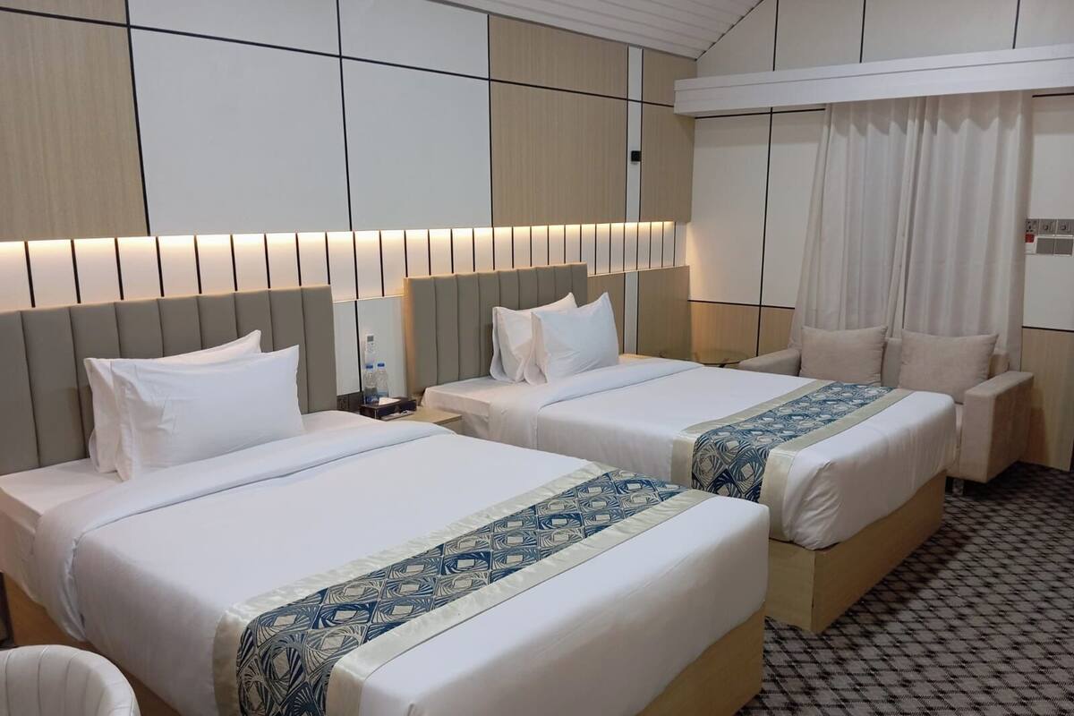 A hotel room with two beds, a chair, a nightstand, and a large window with curtains.