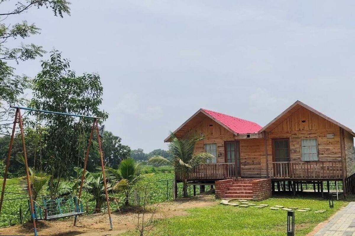 A wooden house with a red roof, a porch, and a small garden area.