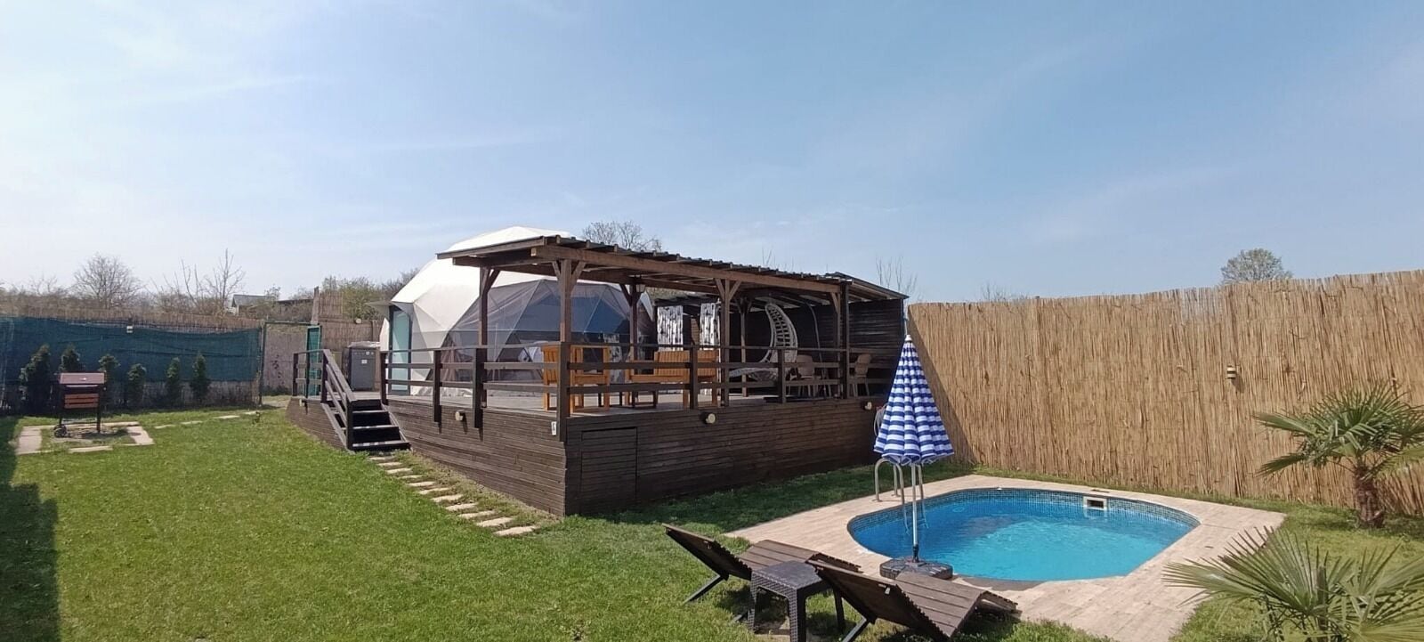 A wooden deck with a covered area, a swimming pool, and a blue-striped umbrella.