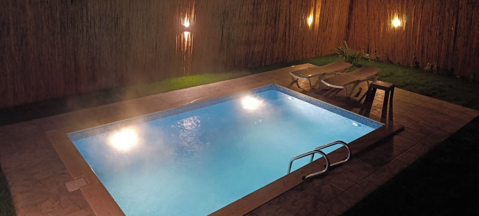 A swimming pool with a wooden deck, lounge chairs, and a wooden wall backdrop.
