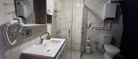 A bathroom with a sink, mirror, shower, toilet, and a towel rack.