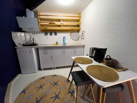 A compact kitchen with a refrigerator, sink, and a coffee maker. There is a dining table with two chairs and a round rug with a star pattern.