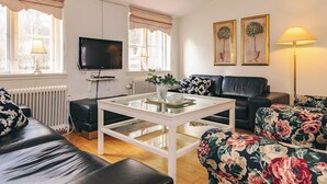 Un salon avec un canapé, une table basse, un téléviseur et deux fenêtres avec des rideaux.