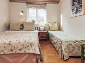 Ein Schlafzimmer mit zwei Betten, einem Heizkörper, einem Fenster mit Vorhängen und einer Lampe.