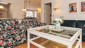 Un salon avec un canapé à motifs floraux, une table basse en verre, un canapé en cuir noir et des lampes fixées au mur.