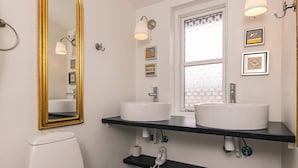 Une salle de bain avec deux lavabos, des toilettes, un miroir avec un cadre doré et une fenêtre agrémentée de rideaux à motifs.