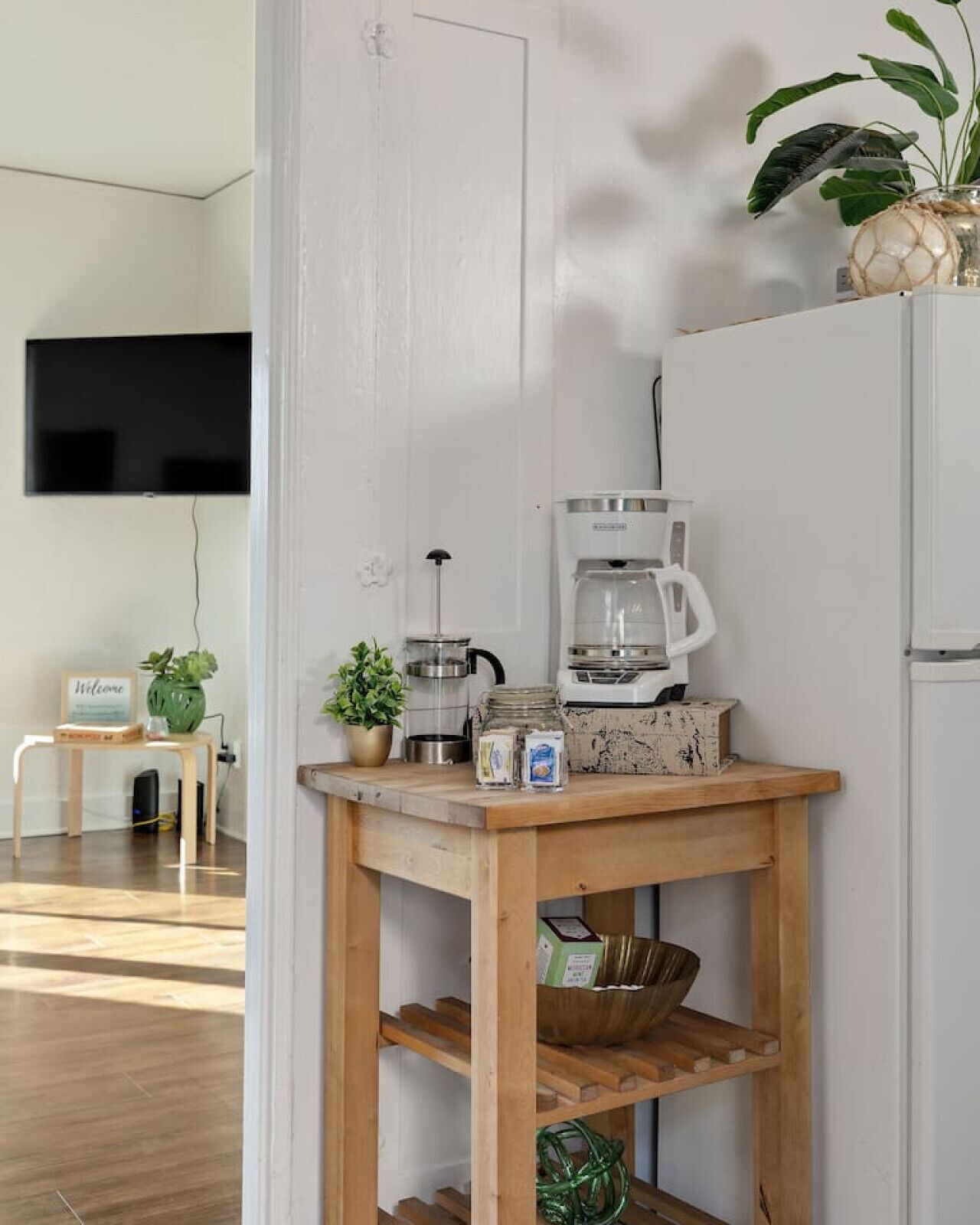 Eine Küche mit Kaffeemaschine, Kühlschrank, einem Holztisch und einem an der Wand befestigten Fernseher.