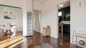 Een ruime woonkamer met een eettafel, stoelen, een groot raam en een zichtbare keuken door een open deur.