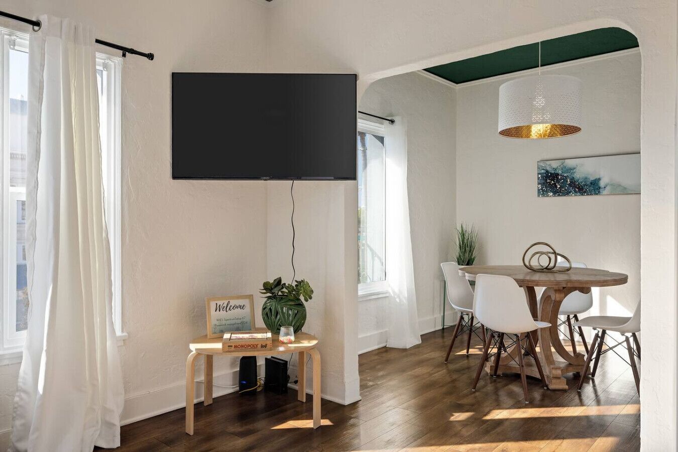 Et værelse med et fladskærms-TV, et bord med stole, en plante og et velkommenskilt.