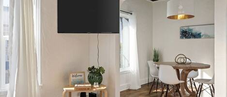 Et værelse med et fladskærms-TV, et bord med stole, en plante og et velkommenskilt.