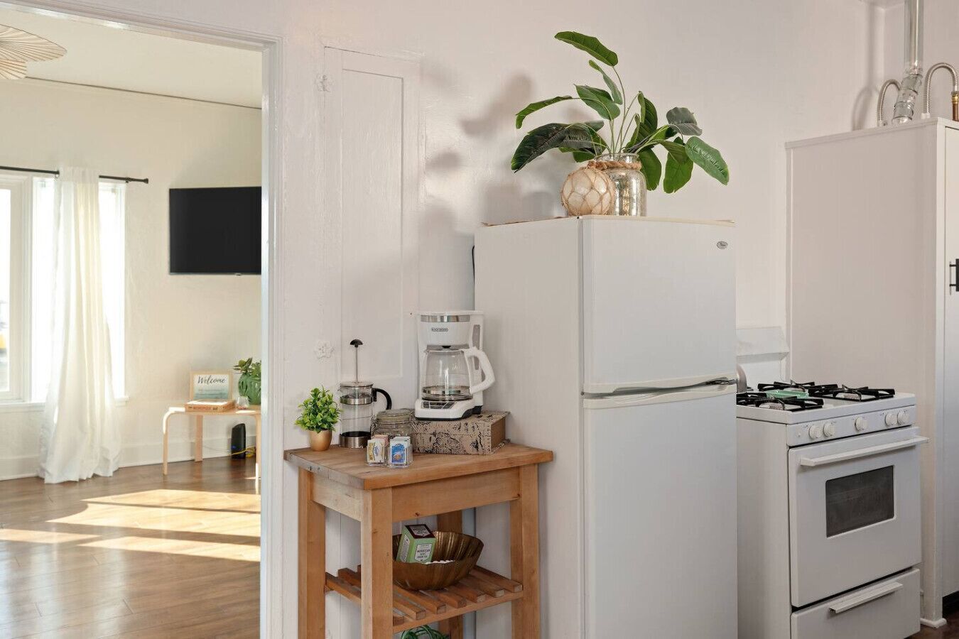 Une cuisine équipée d’un réfrigérateur, d’une cuisinière, d’une machine à café et d’une petite table agrémentée d’une plante et de quelques objets.