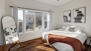 Een slaapkamer met een bed, een plafondventilator, een raam met gordijnen en kunst aan de muur.