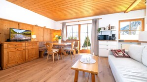 Un interior de madera con televisor, mesa de comedor, sillas, sofá y zona de cocina.