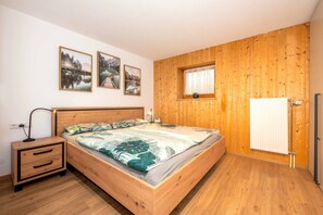 A bedroom with a wooden bed, a nightstand, a window with a view, and a radiator. - BergAusZeit Vacation Apartment (Reit im Winkl)