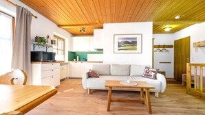 Un salón acogedor con techo de madera, un sofá, una mesa de centro y una cocina al fondo.