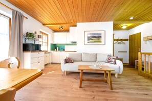 A cozy living area with a wooden ceiling, a sofa, a coffee table, and a kitchen in the background. - Vacation apartment BergAusZeit (Reit im Winkl)