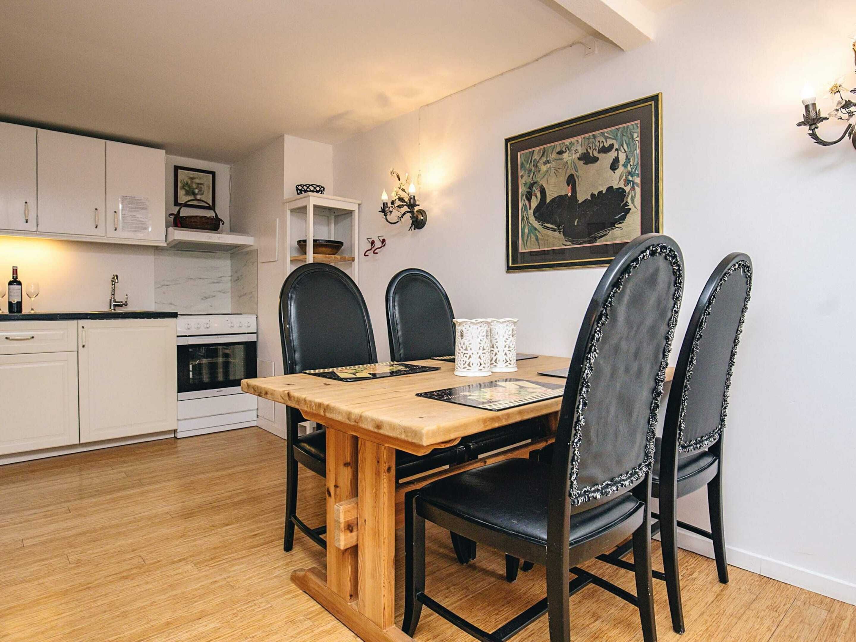 Un coin repas comprenant une table en bois, des chaises noires, un meuble blanc et un luminaire fixé au mur.