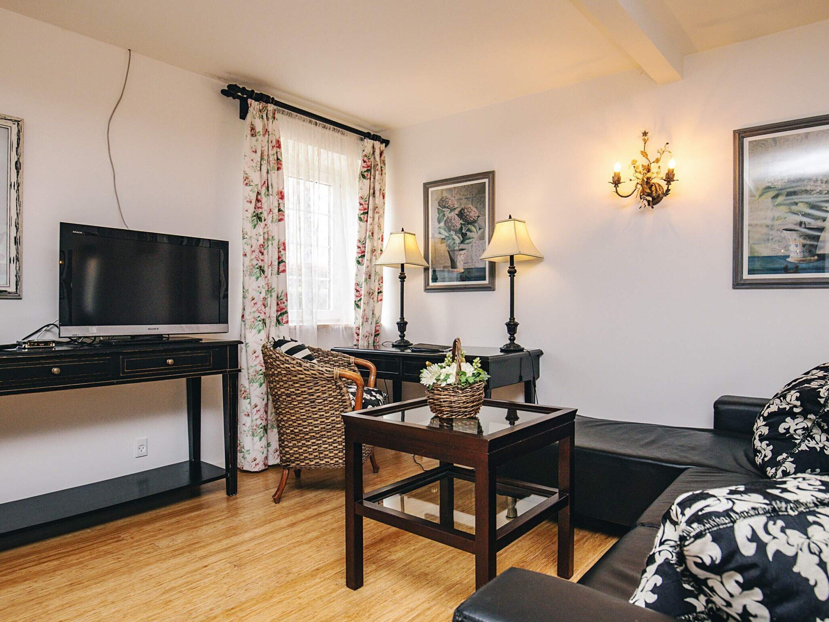 A living room with a television, a sofa, a coffee table, a wicker chair, and a lamp.