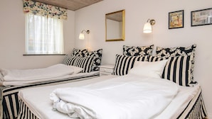 Ein Zimmer mit zwei Betten, einem Vorhangfenster, einem Spiegel, Wandleuchten und gerahmten Bildern.