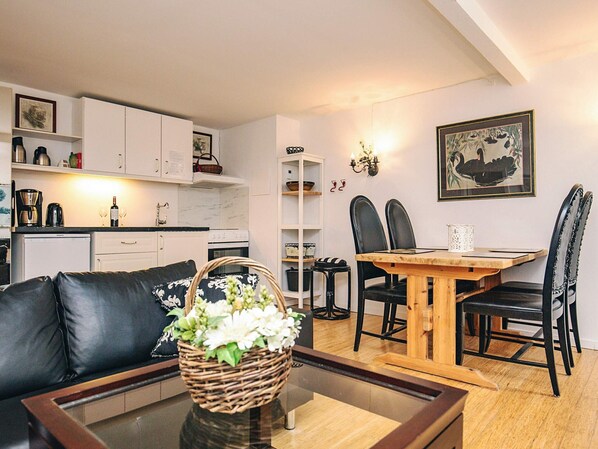 A modern living room with a glass coffee table, a black leather sofa, a dining table with four chairs, and a kitchen in the background. - 4 Person Holiday Home in Brovst (Brovst)