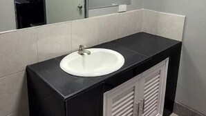 A bathroom with a white sink, black vanity, a mirror, and a trash bin. - Dan Mai Homestay  (Ko Chang)