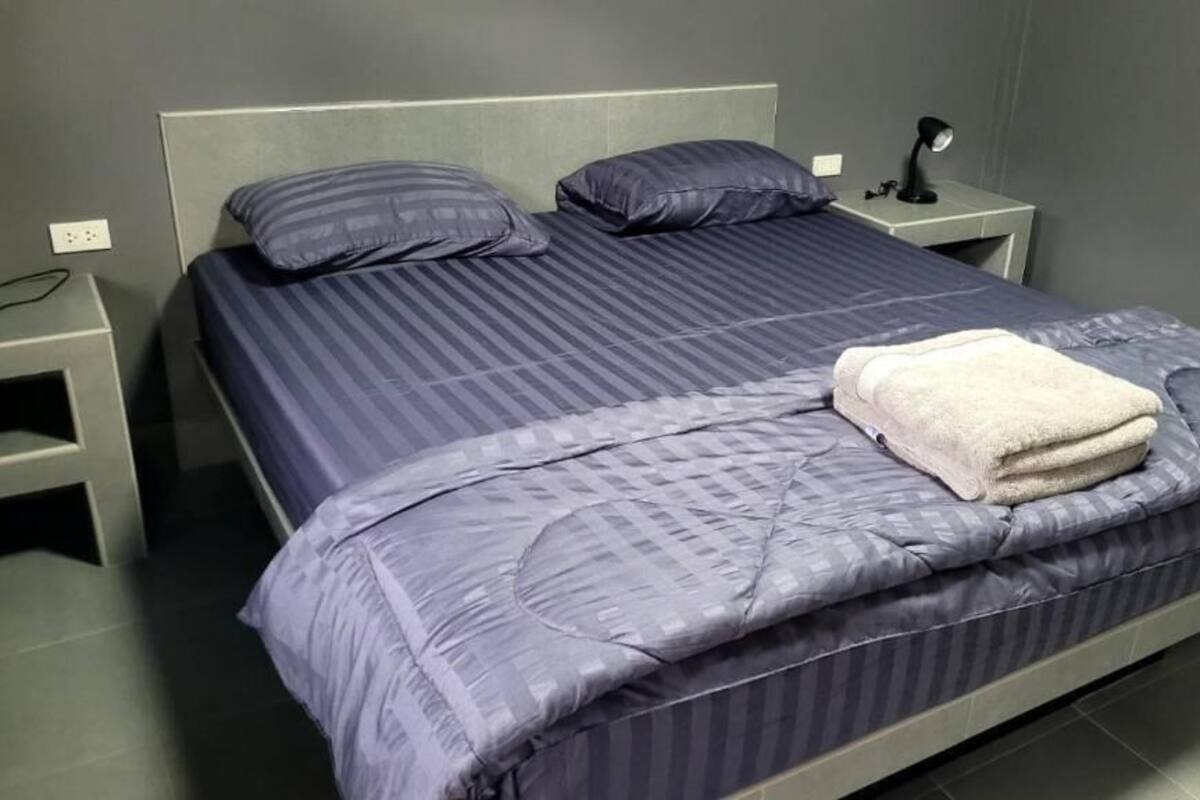 A bed with a striped bedspread, two pillows, a bedside lamp, and a folded towel on the bed.