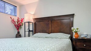 Un lit bien fait, recouvert d’une couvre-lit à motifs, une table de chevet ornée d’un vase de fleurs et une petite table de nuit avec une lampe.