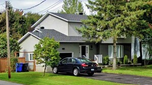 Une maison d’habitation avec une allée, une voiture garée et un petit arbre dans le jardin.