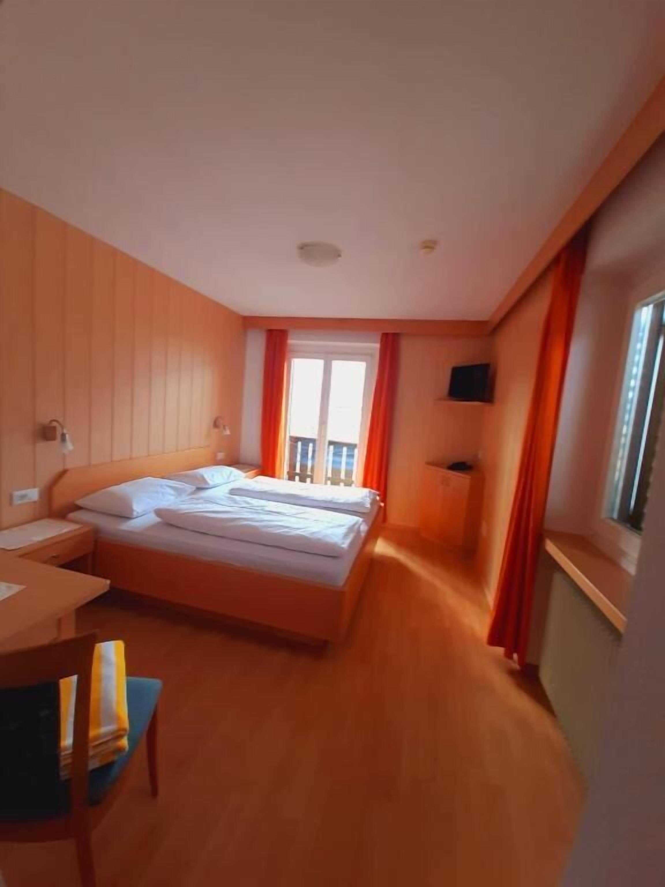 A hotel room with a bed, a desk, a chair, a TV, and a window with curtains.