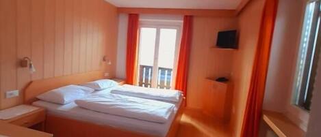 A hotel room with a bed, a desk, a chair, a TV, and a window with curtains.