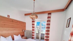Un dormitorio con cama y escritorio de madera, un radiador y una ventana con cortinas.