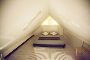 A small, triangular attic bedroom with a sloped ceiling, a bed with pillows, and a wooden bench. - Les 2C' House 200m from the beach (Cayeux-sur-Mer)