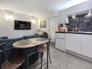 A compact living space with a kitchenette, a dining area with a table and chairs, a sofa, and a television mounted on the wall. - 1 bedroom accommodation in Kilsyth (Kilsyth)