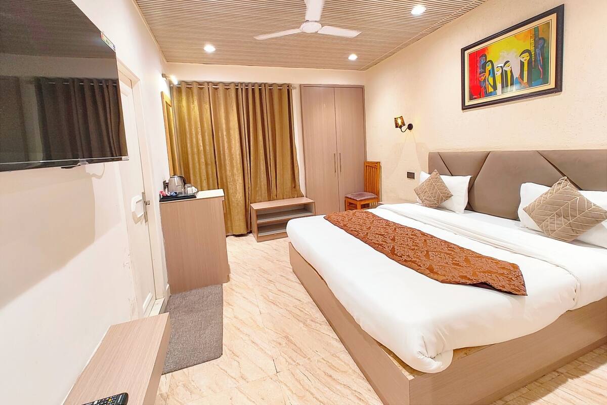 Ein Hotelzimmer mit Bett, Schreibtisch, Stuhl, Kleiderschrank, Deckenventilator und einem Bild an der Wand.
