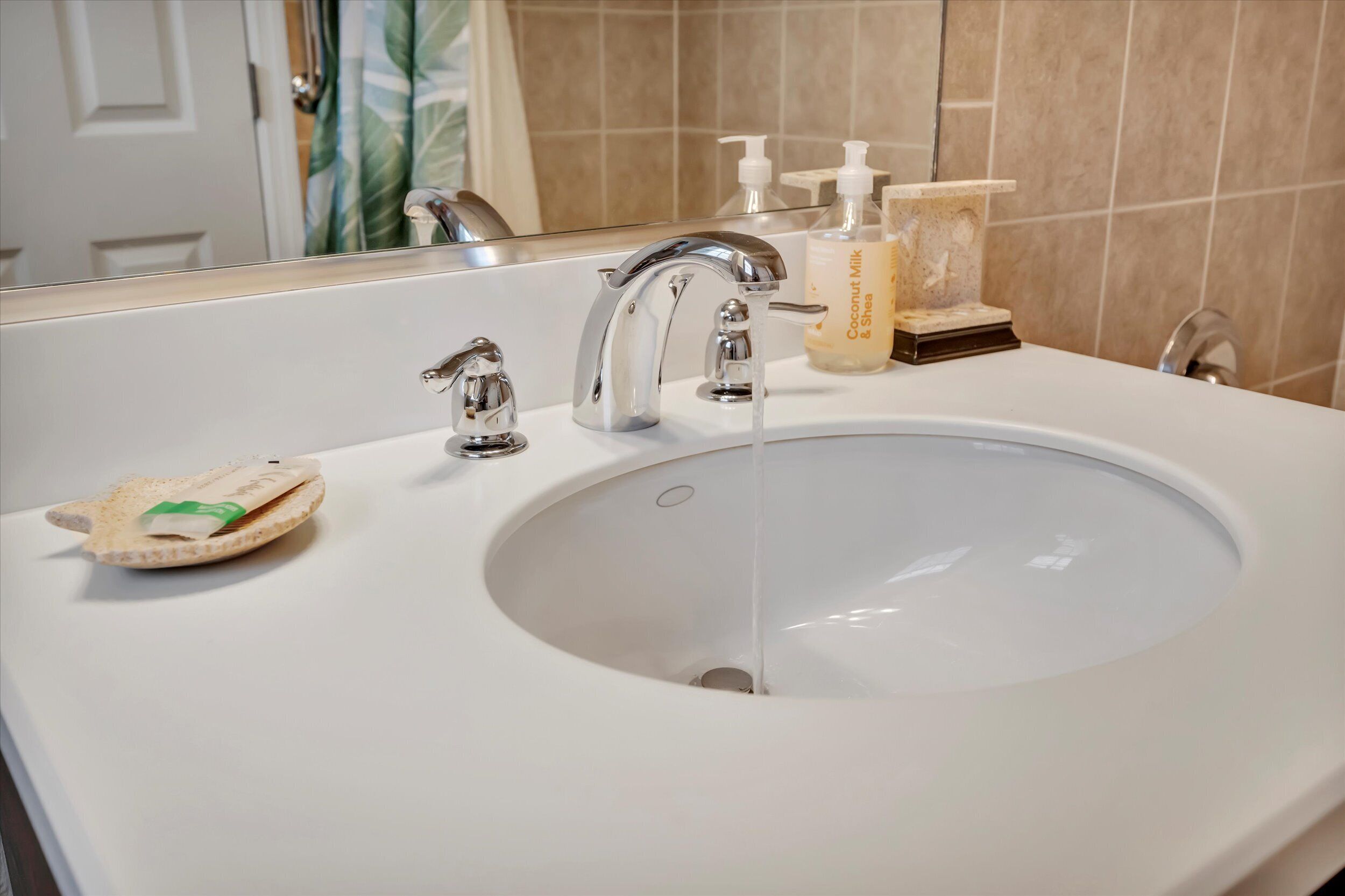 A bathroom with a white sink, two faucets, a mirror, and toiletries on the counter.
