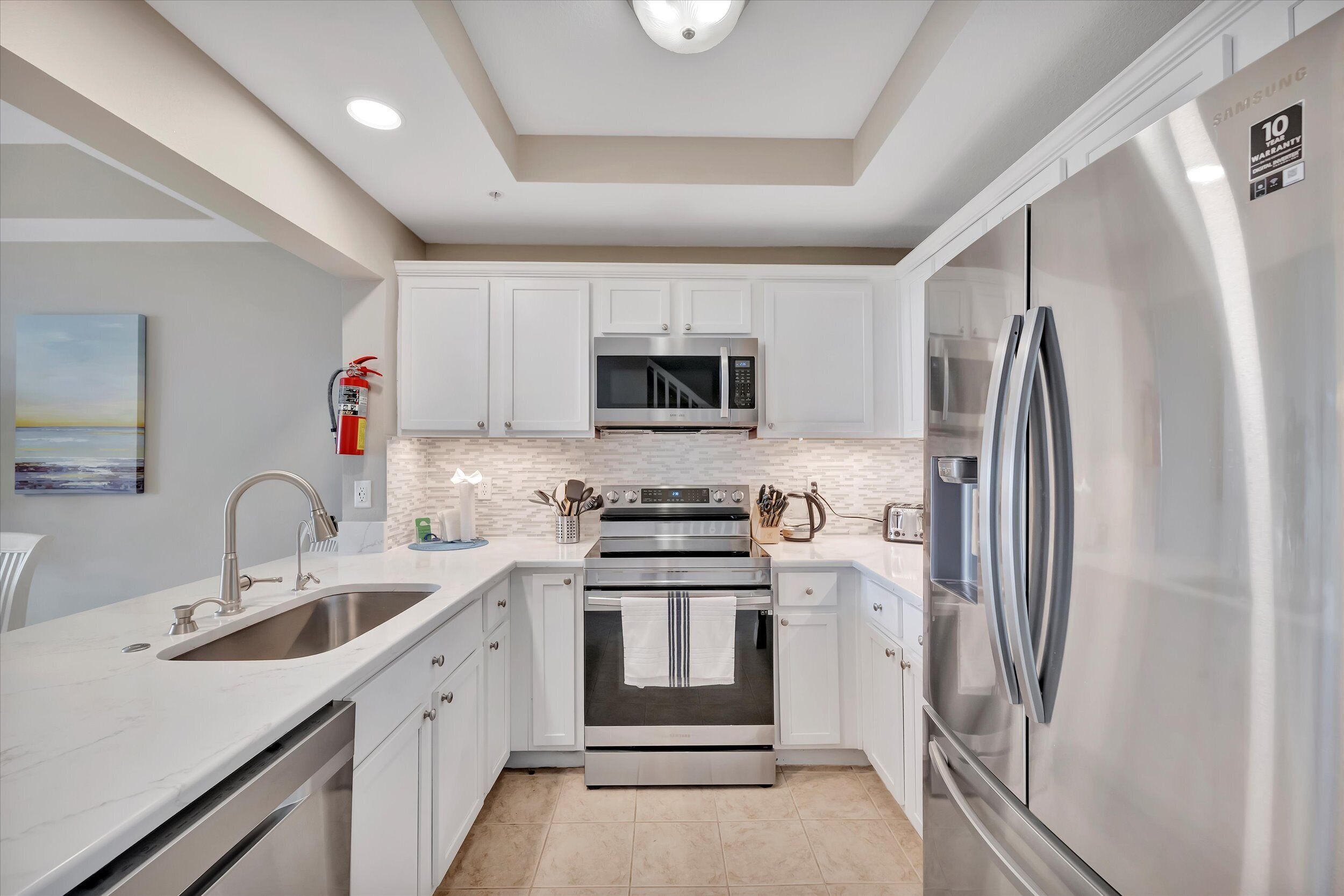 A modern kitchen with stainless steel appliances, white cabinetry, and a tiled backsplash.