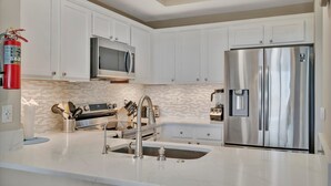 A modern kitchen with white cabinets, stainless steel appliances, a microwave, and a refrigerator. - Mangrove Point Townhome (Ruskin)