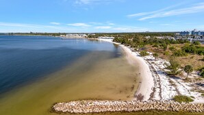 A coastal beach with a rocky shoreline, clear water, and a distant view of buildings. - Mangrove Point Townhome (Ruskin)