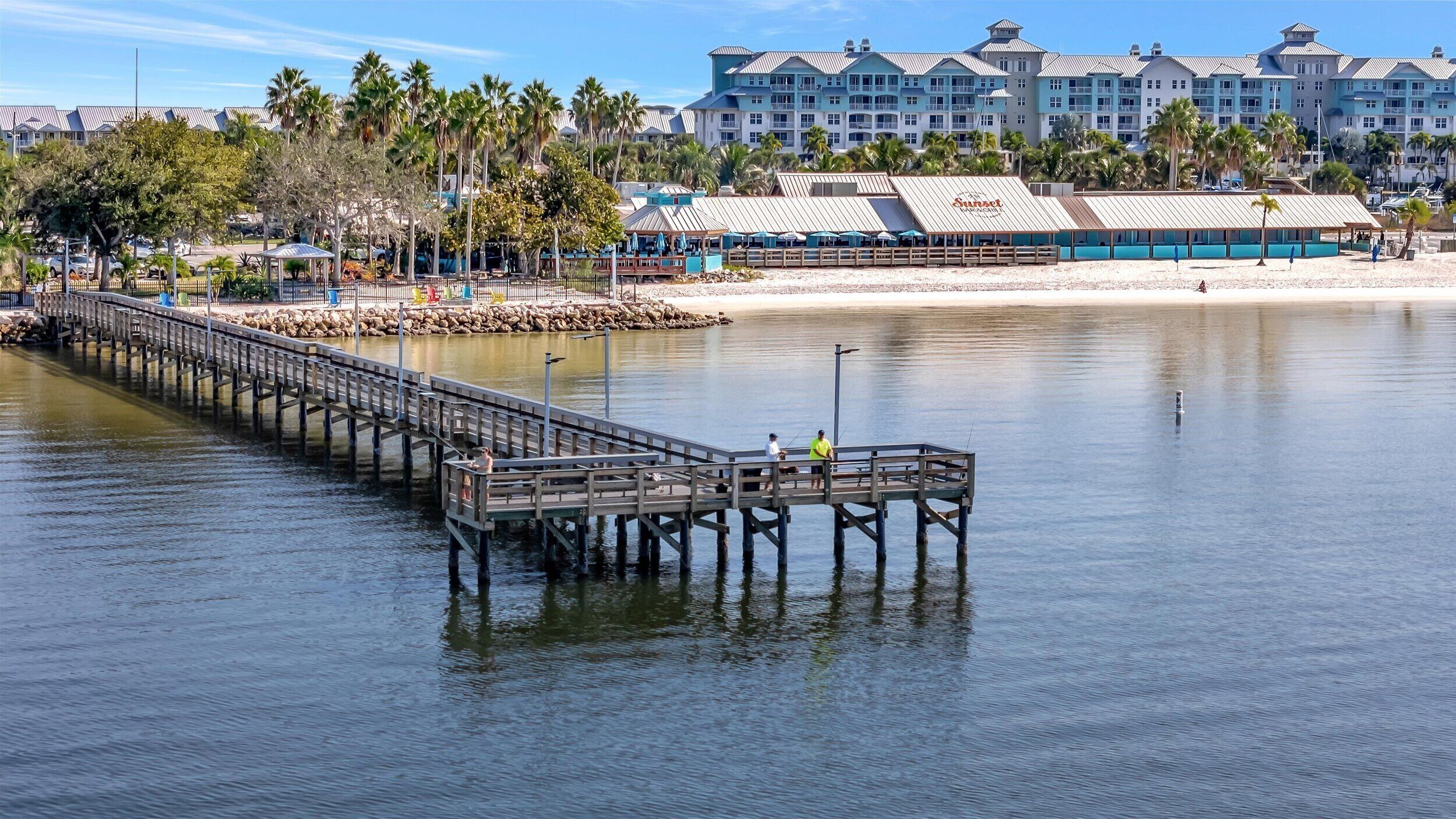 Eine Steg, der sich ins ruhige Wasser erstreckt, mit einem Strand und Hotelgebäuden im Hintergrund.